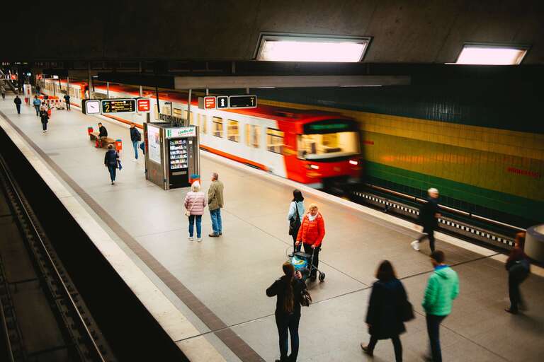 Pessoas na estação de metrô, com trem vermelho chegando.